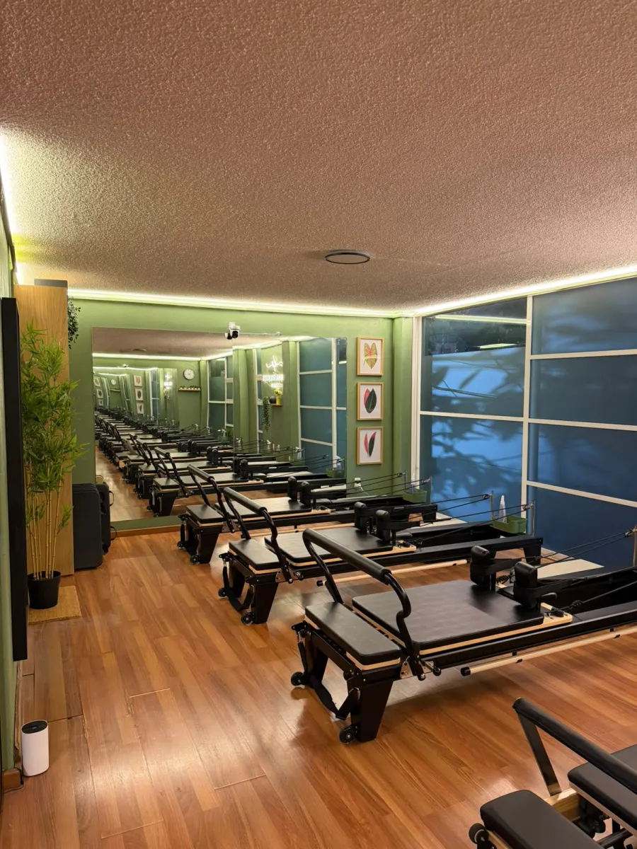 Sala de pilates reformer con piso de madera y cuadros botánicos